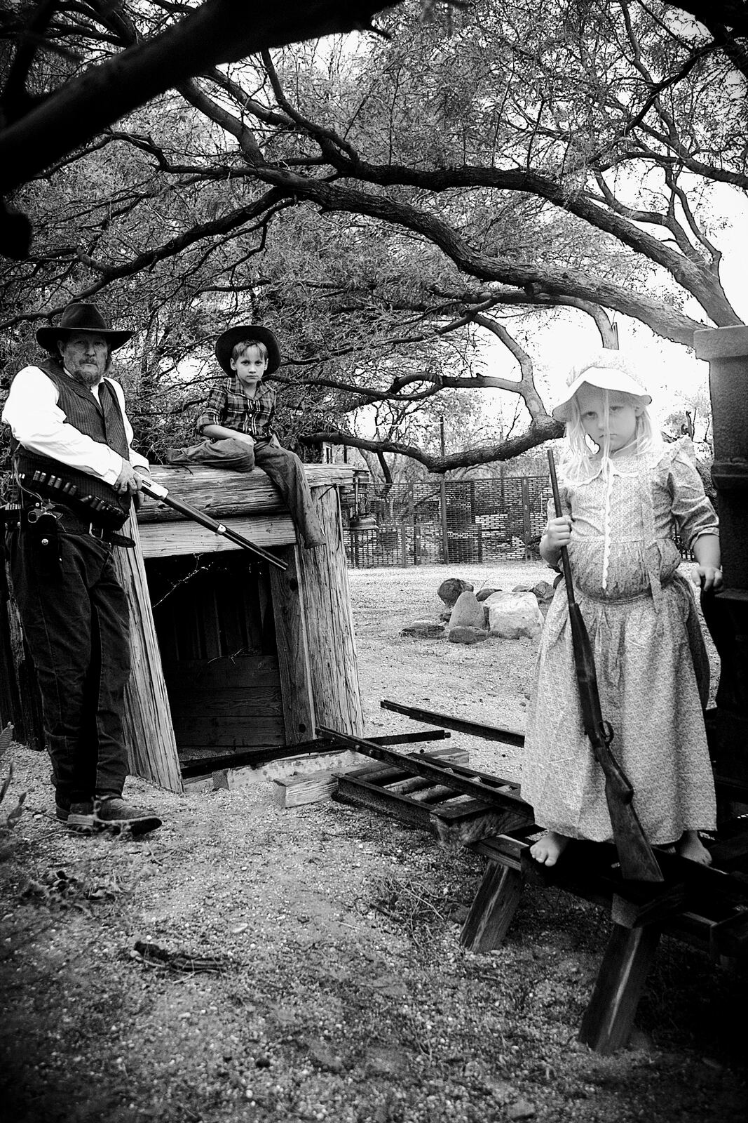 Man and two children in Old Western outfits posed by a wooden mine entrance