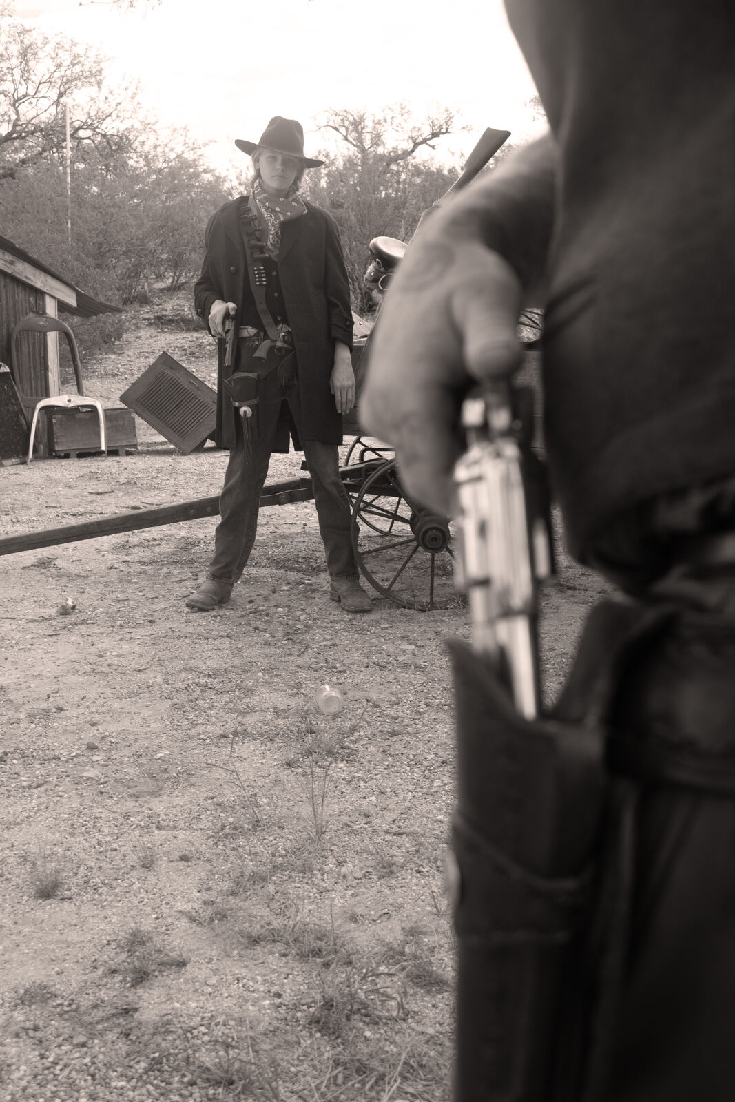 Cowboy in a hat standing on a dirt road with a revolver in the foreground