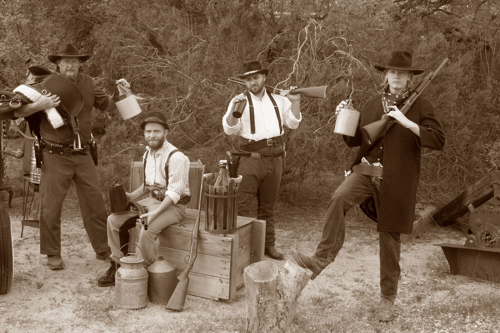 Group of five in Old Western outfits posed among crates and milk cans