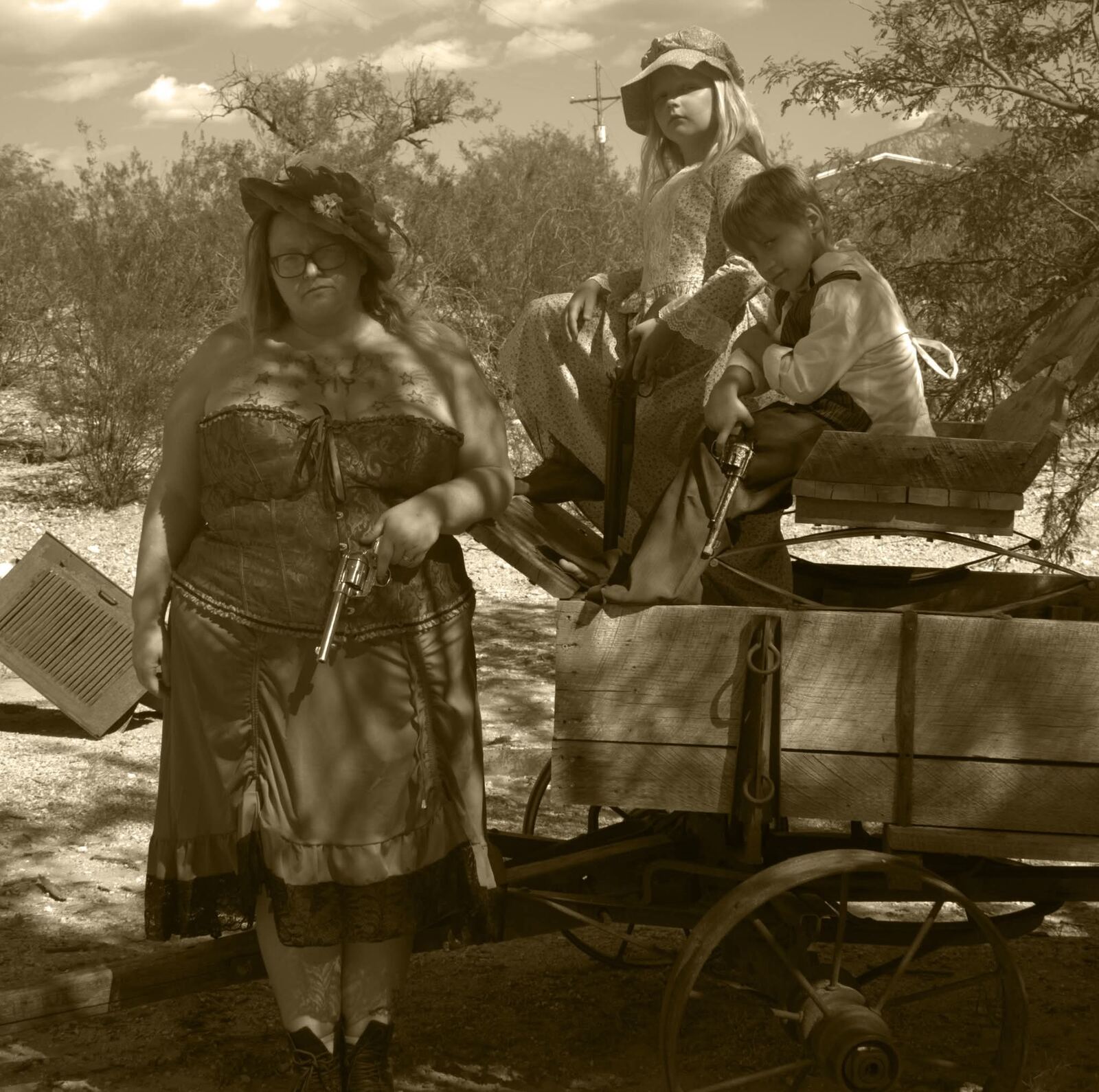 Woman in a corset dress and two children posed beside a wagon