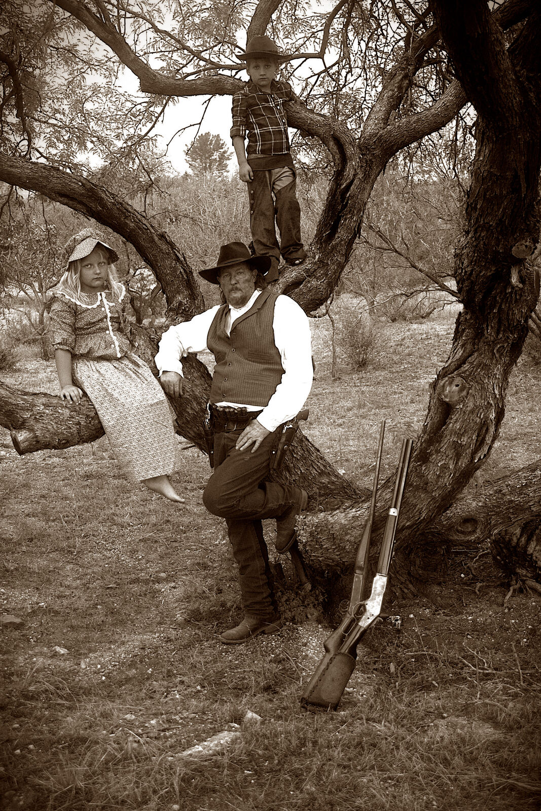 A family in Old Western outfits posed in and around a mesquite tree
